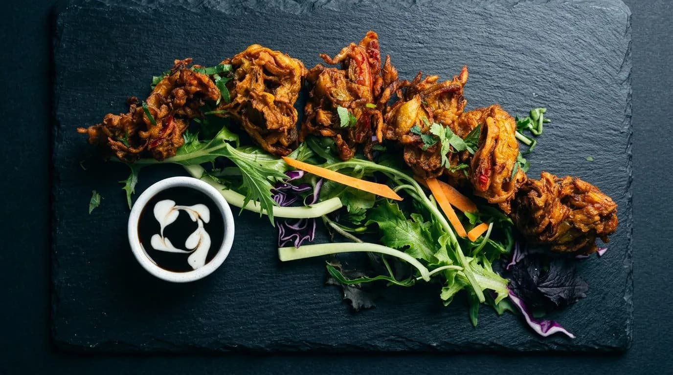 Crisp onion fritters on a slate board with salad and a dipping sauce.